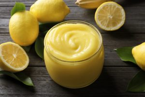 Citronkräm i glasburk med färska citroner på träbord.
