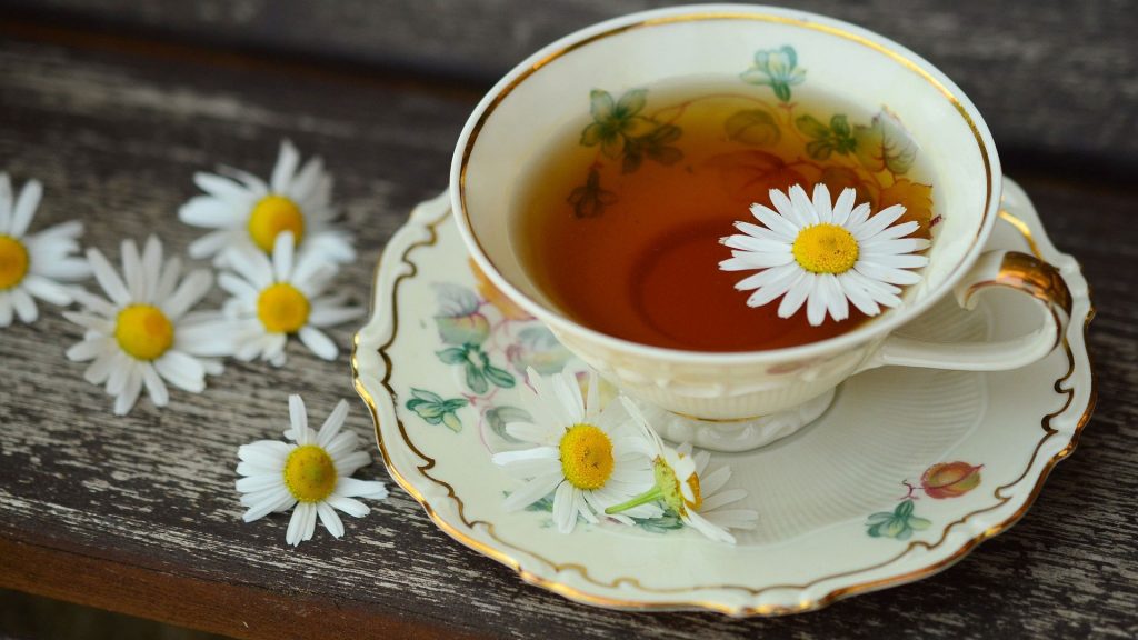 Porslinskopp med kamomillte och blommor på träbord.