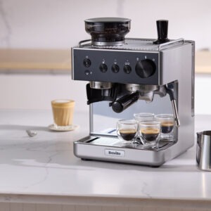 Espressomaskin på köksbänk i stilren design, med koppar och kaffemjölkskanna.