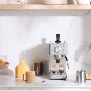 Espressomaskin med juice och päron på modern köksbänk.