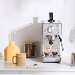 Espressomaskin med juice och päron på modern köksbänk.