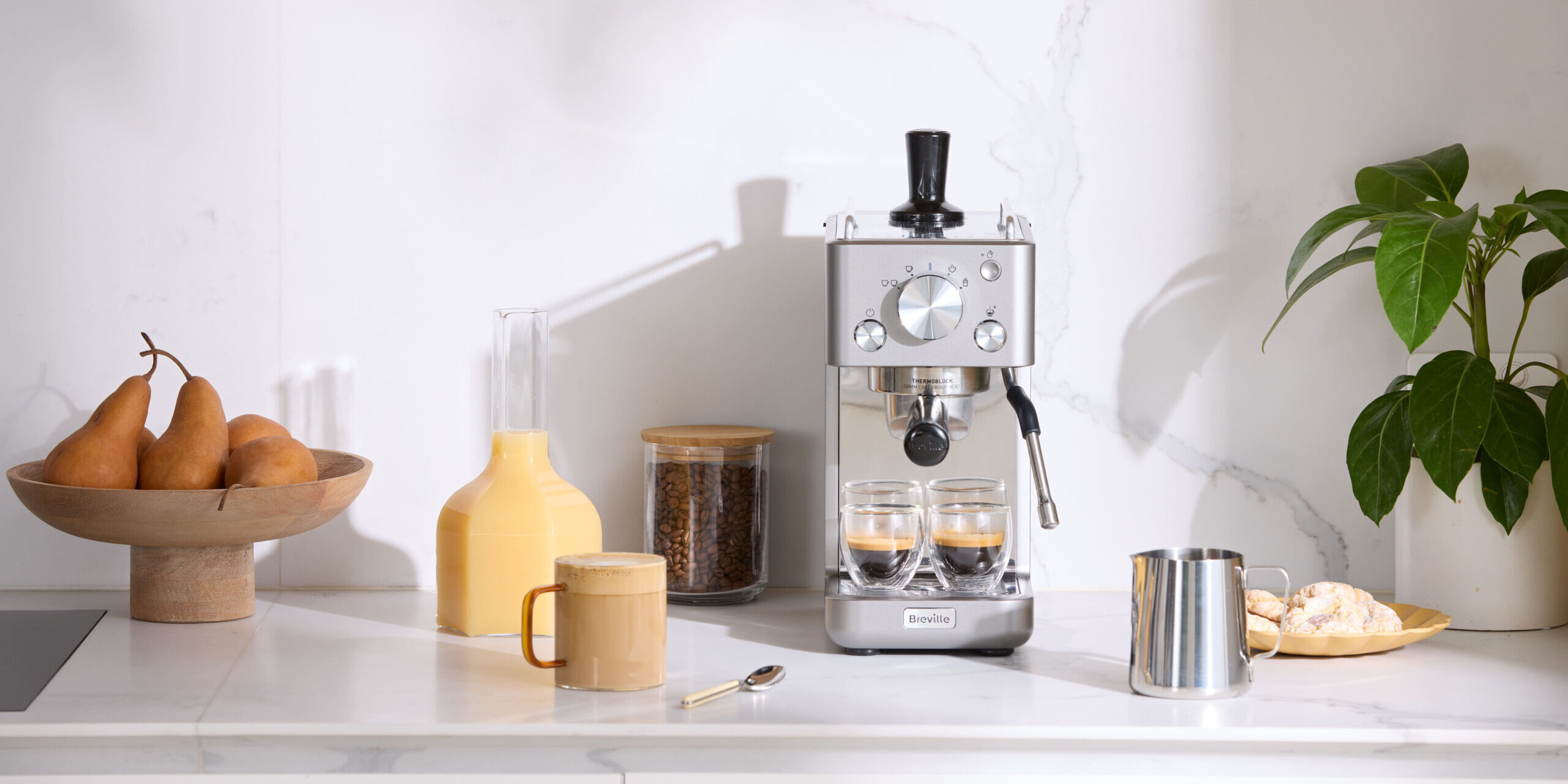 Espressomaskin med juice och päron på modern köksbänk.