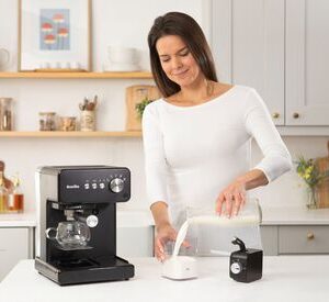 Kvinna gör kaffe i kök med espressomaskin och mjölk.