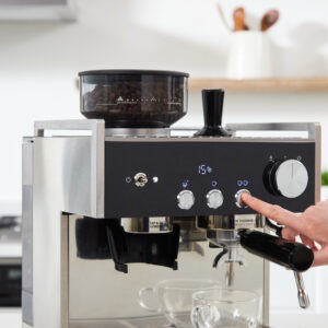 Modern espressomaskin i köket med person som trycker på en knapp.