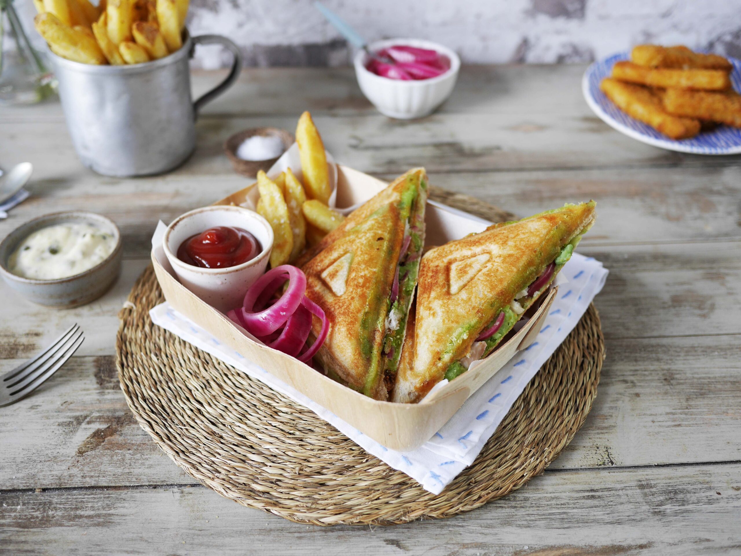 Grillade smörgåsar med pommes frites, ketchup och picklad rödlök serverade på en träbricka.
